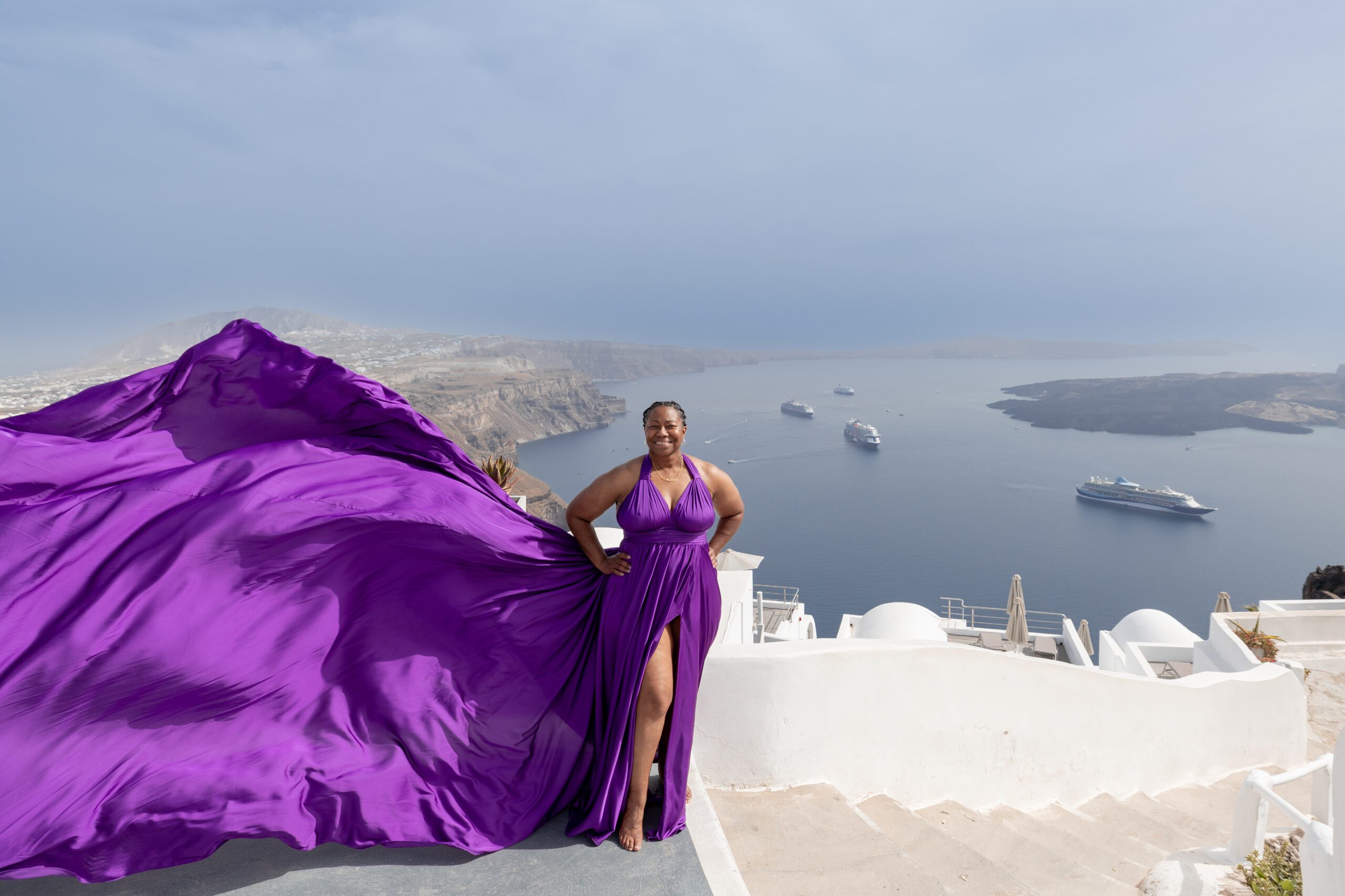 Woman in purple flowing dress posing against Santorini white architecture and blue sky