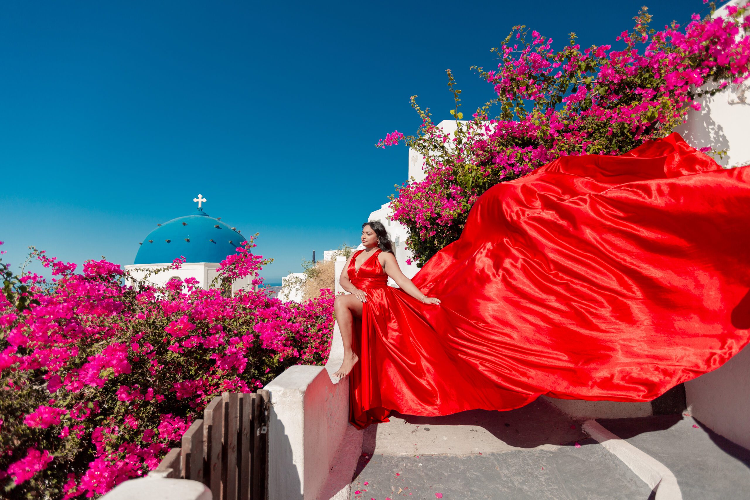 Red flying dress photoshoot in Santorini — dramatic fabric flow against the Aegean sea