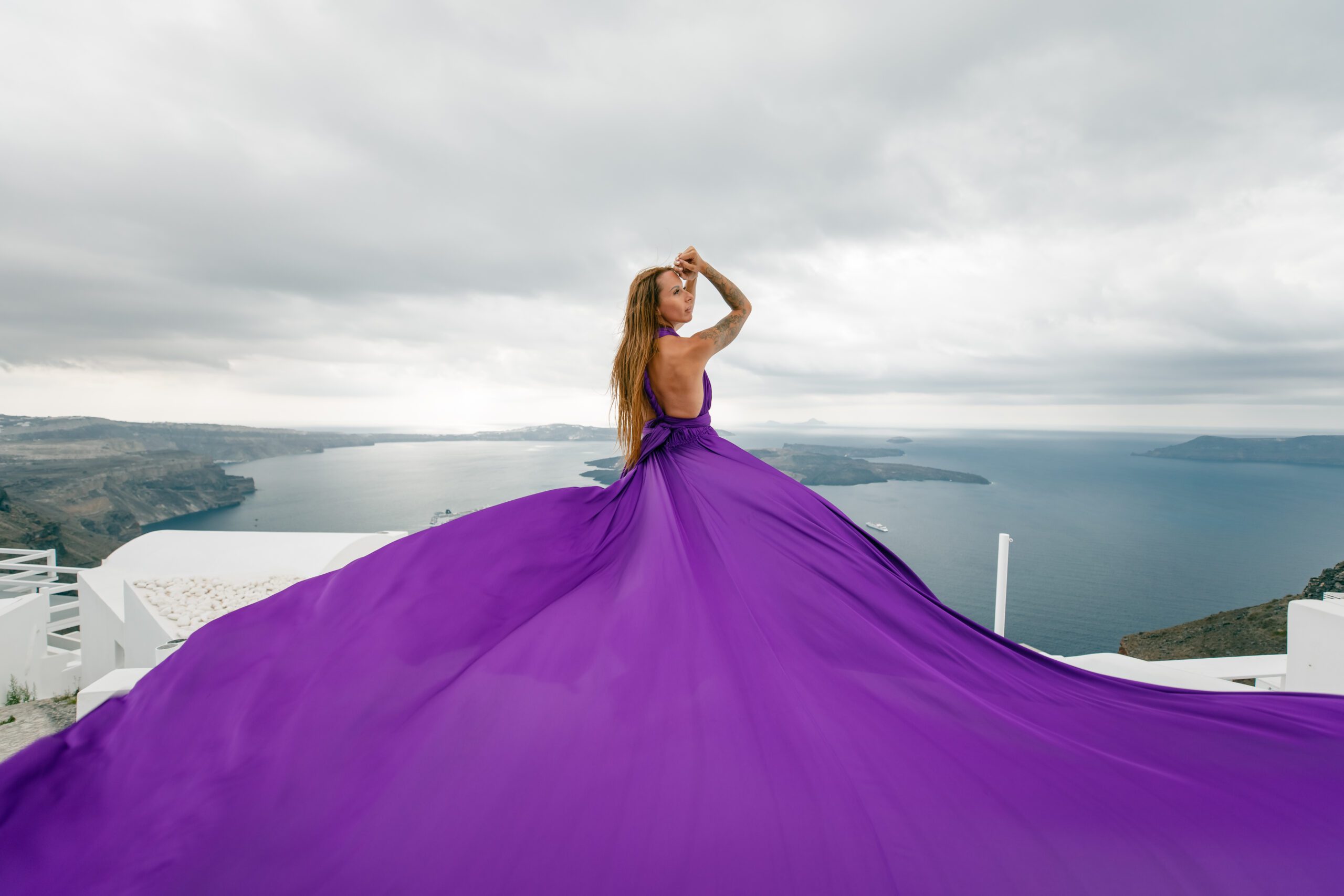 Santorini flying dress photo session in violet — vibrant color against iconic white-washed walls